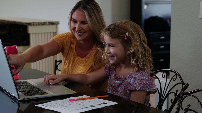一位母亲和她的女儿在网上上课时指着电脑屏幕