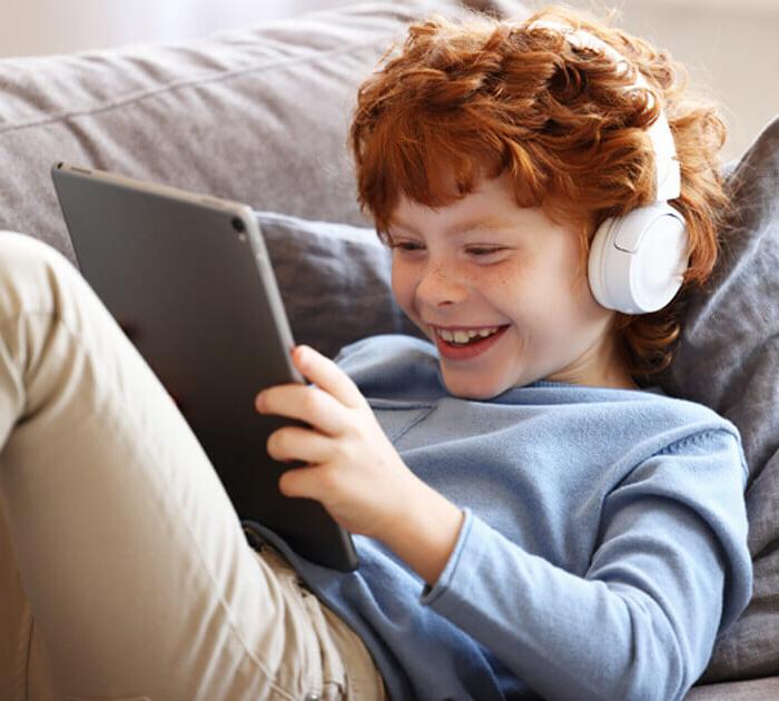 一个小男孩听着耳机，对着他的平板电脑微笑